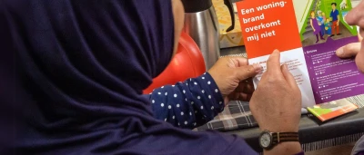 Een persoon met een hoofddoek houdt een brochure vast, terwijl een andere hand ook leest.