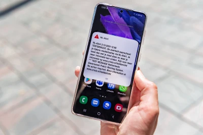 Een hand houdt een smartphone met een NL-Alert testbericht op het scherm.