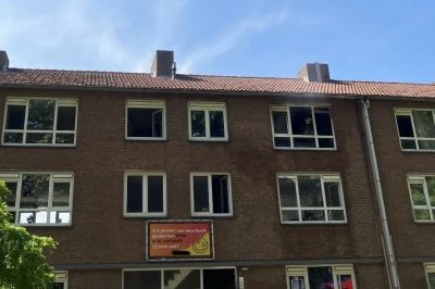 Verschillende ramen van een stenen gebouw met een heldere blauwe lucht en bomen.
