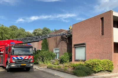 Brandweerwagen met ladder naast een modern bakstenen huis onder een blauwe lucht.