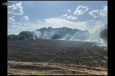 Rook stijgt op boven een verbrand veld onder een heldere lucht met wolken.