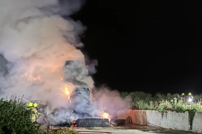 Vlammen en rook stijgen op in de duisternis, bij een brand op een bouwplaats.
