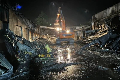 Een zwaar beschadigd gebouw met een graafmachine, verlicht in de nacht.