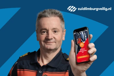 Man in uniform houdt smartphone vast met een app, gefotografeerd tegen een blauwe achtergrond.