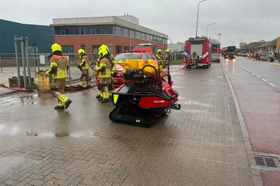 Brandweermensen in gele helmen bij een voertuig op een natte straat.
