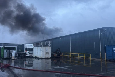 Zwart rook stijgt op boven een industriëel gebouw op een bewolkte dag.