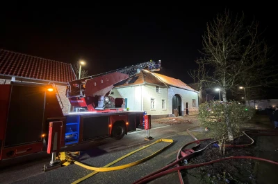 Brandweerwagen met ladder voor een gebouw, 's nachts verlicht door straatlantaarns.