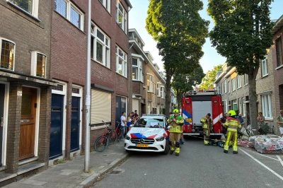 Brandweer en politie op een straat, mensen kijken toe, bomen in de achtergrond.
