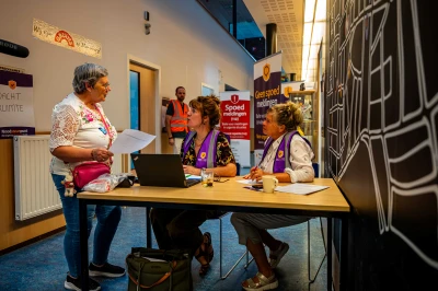 Drie mensen aan een tafel in een lichte ruimte, met informatie en computers.