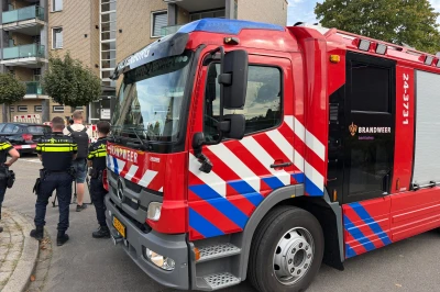 Rood brandweerwagen geparkeerd op straat met politieagenten in gesprek.