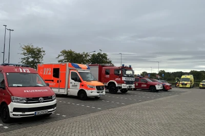 Een rij hulpvoertuigen, waaronder ambulances en brandweerwagens, geparkeerd onder een bewolkte lucht.