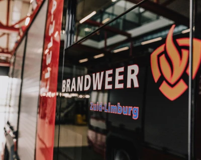 Zijaanzicht van een brandweerwagen met het woord 'BRANDWEER' en een logo.