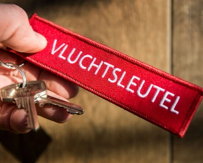Rode sleutelhanger met het woord "VLUCHTSLEUTEL" en een paar metalen sleutels.