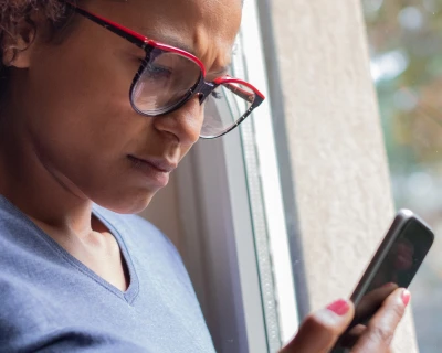 Vrouw met een frons kijkt gefocust naar haar smartphone bij een raam.