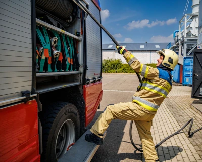 Brandweerman in uniform trekt gereedschap uit brandweerwagen onder een blauwe lucht.