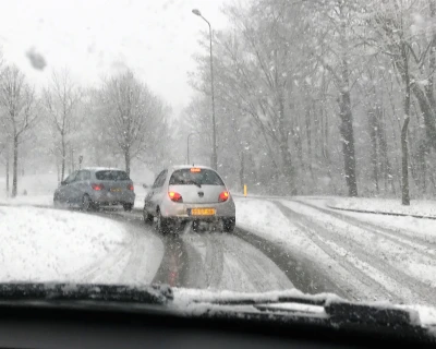 Sneeuw bedekte weg met twee auto’s die voorzichtig draaien in winterse omstandigheden.