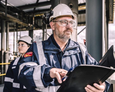 Twee inspecteurs op een industriegebied, een man en een vrouw, met helmen en documenten.